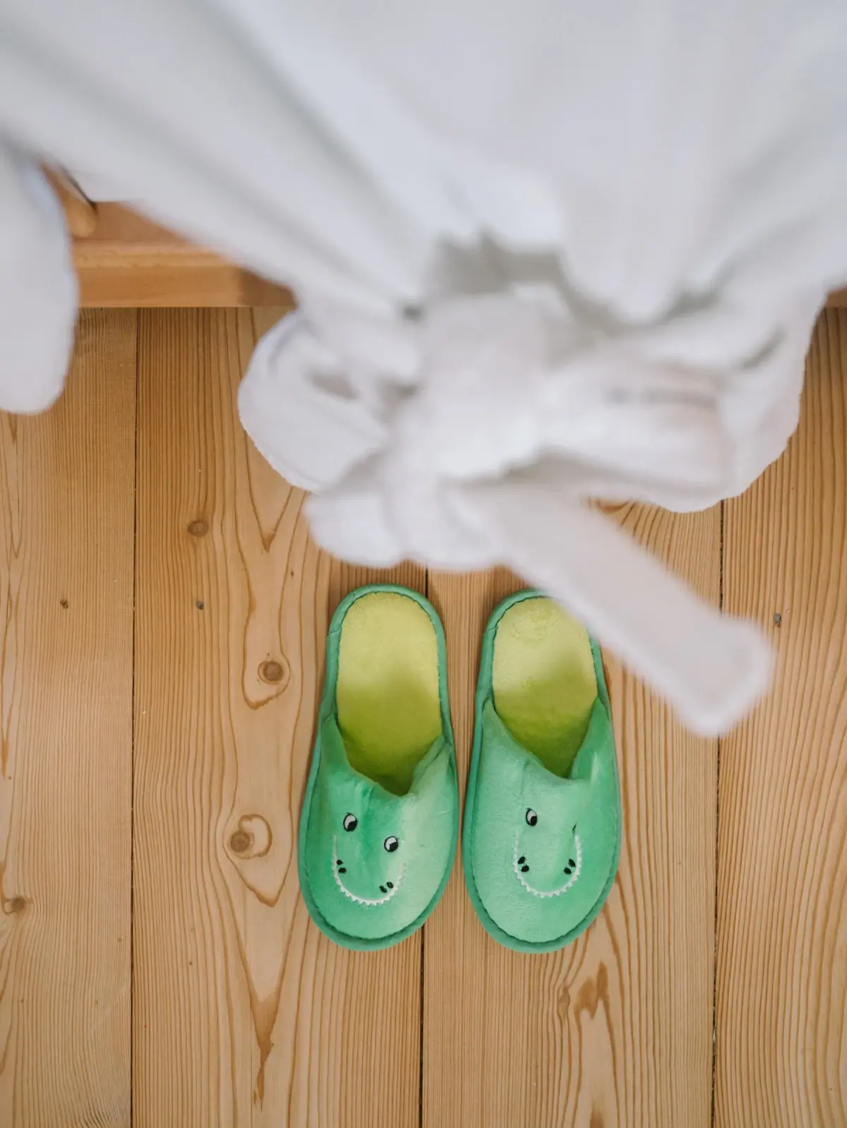 Wellness mit Kind Ein Paar grüne Hausschuhe auf einem Holzboden.