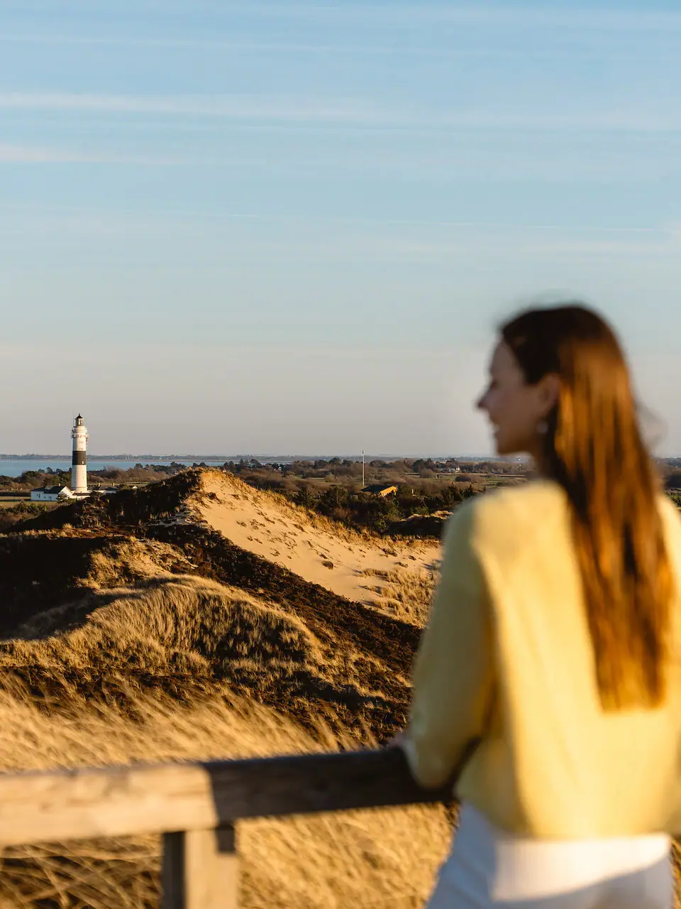 Sylt Eine Frau steht auf einem Zaun und blickt auf einen Leuchtturm auf Sylt.