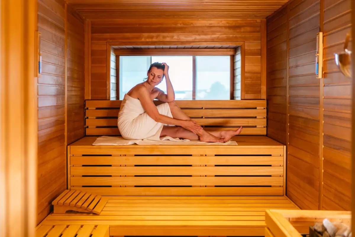 Sauna im A-ROSA Travemünde Eine Frau in einem Handtuch sitzt auf einer Holzbank in einer Sauna.