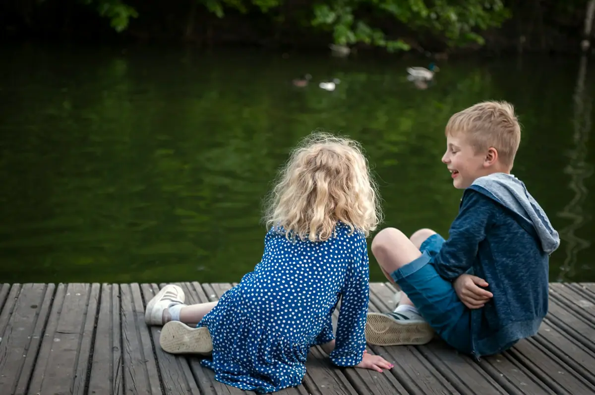Ein Junge und ein Mädchen sitzen auf einem Steg in der Nähe von Wasser.