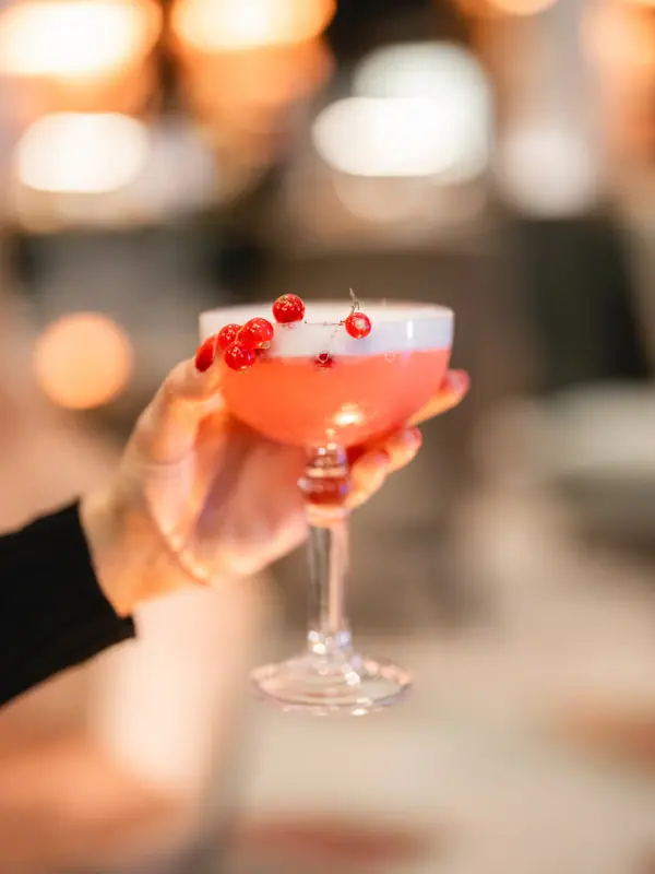 Drink Bar Eine Hand hält ein Glas mit rosa Flüssigkeit.