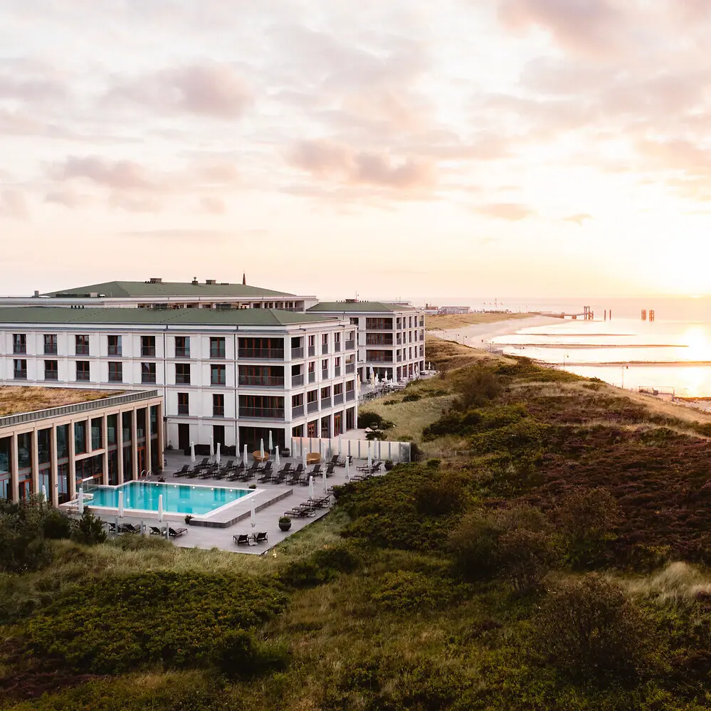 A-ROSA Sylt Das A-ROSA Sylt mit einem Outdoor-Pool an den Dünen mit der Nordsee daneben..