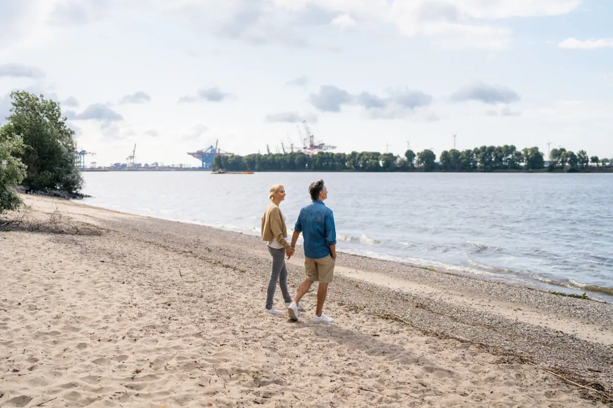 Elbstrand Ein Mann und eine Frau halten sich an den Händen am Elbstrand.