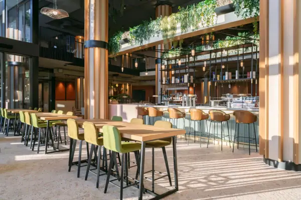 Hotelbar A-ROSA Gardasee Die Bar im A-ROSA Gardasee mit großen Säulen, einer langen Theke sowie Tischen und Stühlen.