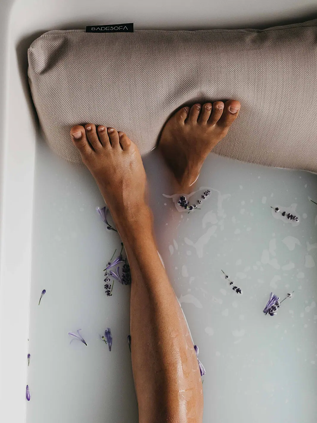 Badesofa Füße einer Person in einer Badewanne mit Milch und Blumen