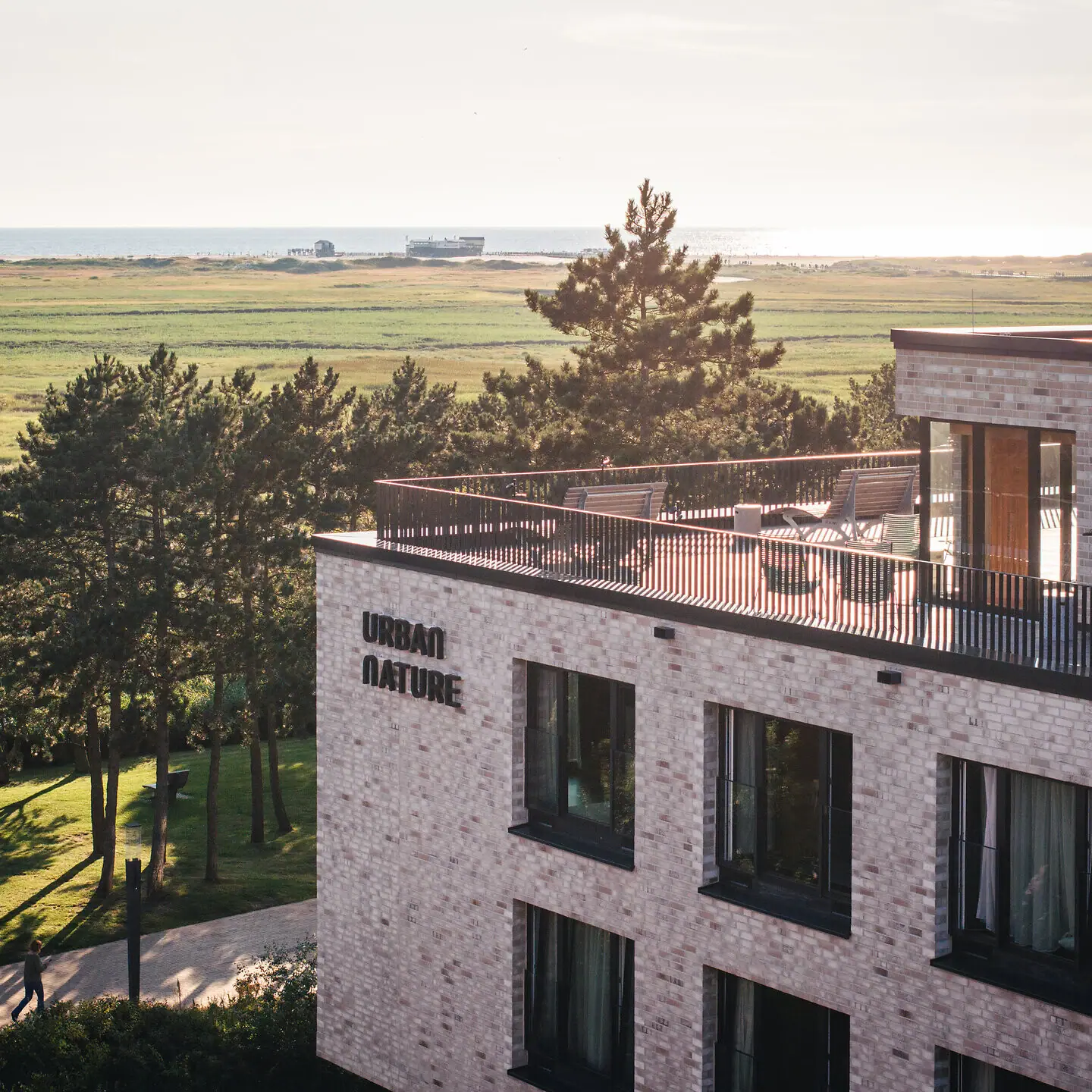 Urban Nature Hotel St. Peter-Ording Ein Gebäude mit einem Balkon, der auf ein grasbewachsenes Feld blickt.