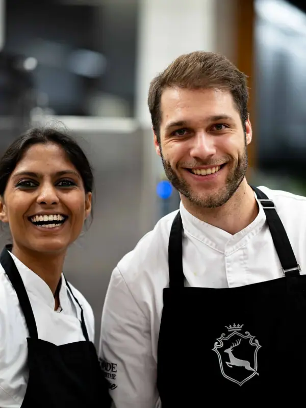 Küchenparty im A-ROSA Ifen Hotel Ein Mann und eine Frau in Schürzen lächeln.