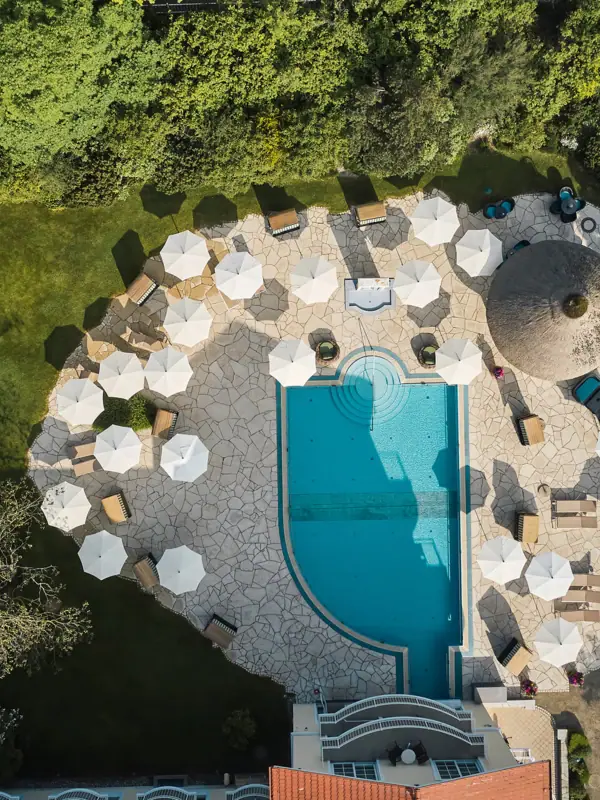 Pool Luftaufnahme eines Pools mit Sonnenschirmen und umgebenden Pflanzen und Bäumen.