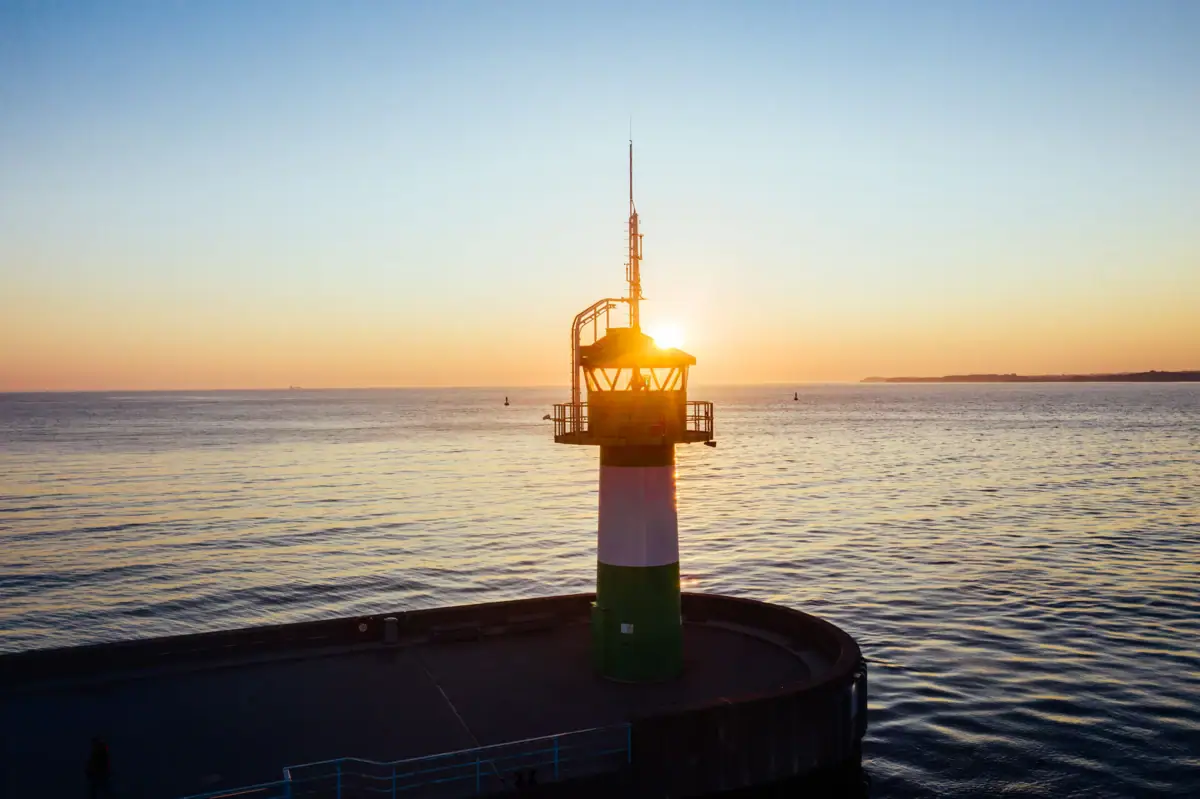 Travemünde Ein Leuchtturm auf einem Steg im Wasser.