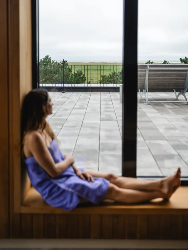 Sauna im Urban Nature Frau sitzt auf einer Fensterbank in der Sauna vom Urban Nature Hotel St. Peter-Ording und schaut aus dem Fenster.