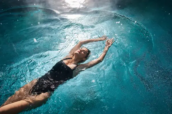Urban Nature Bad Gastein Eine Frau in einem schwarzen Badeanzug treibt in einem Pool.