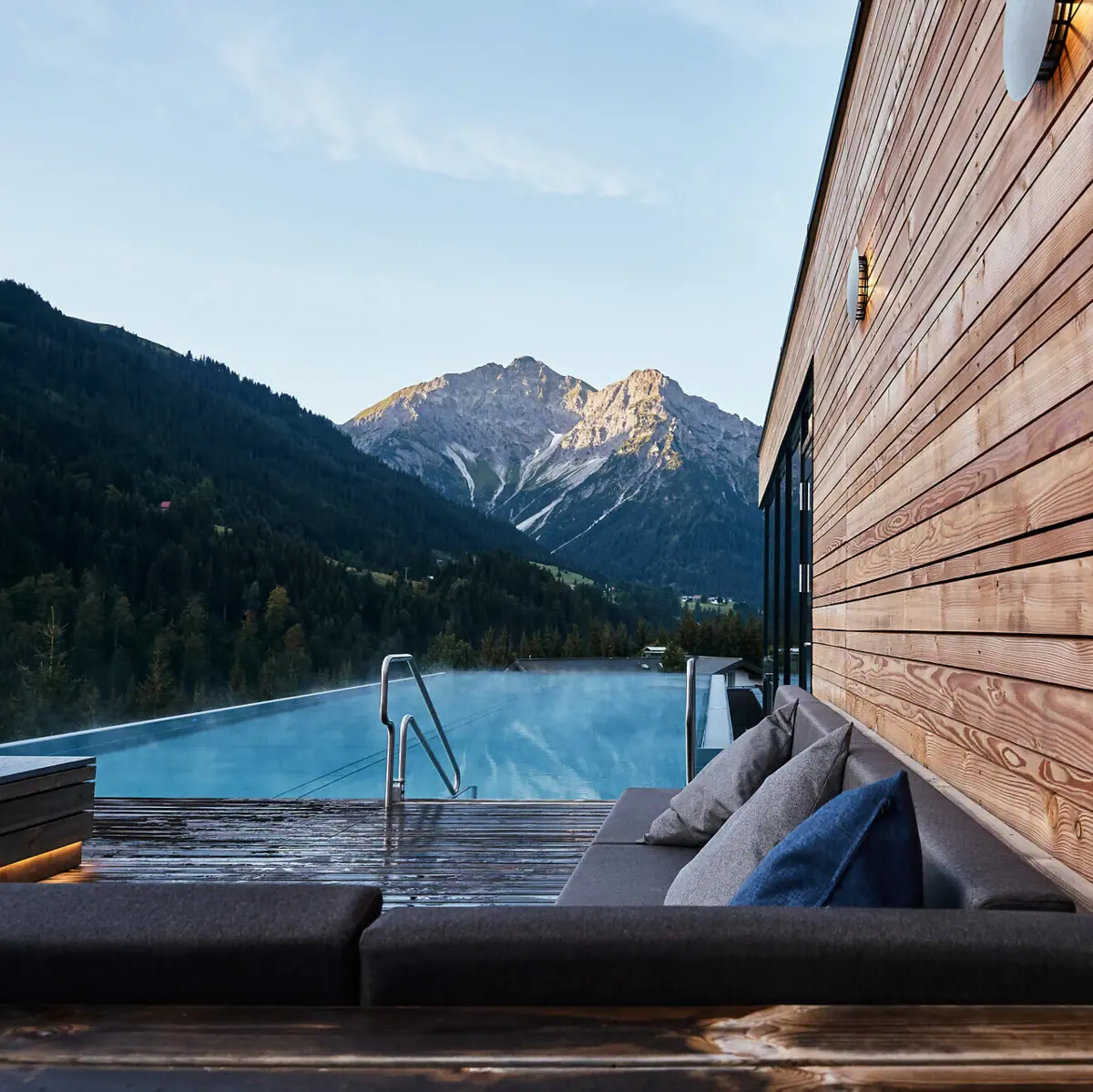 Aussenpool im SPA-ROSA Kleinwalsertal Ein Hotel mit einem Pool und Bergen im Hintergrund.