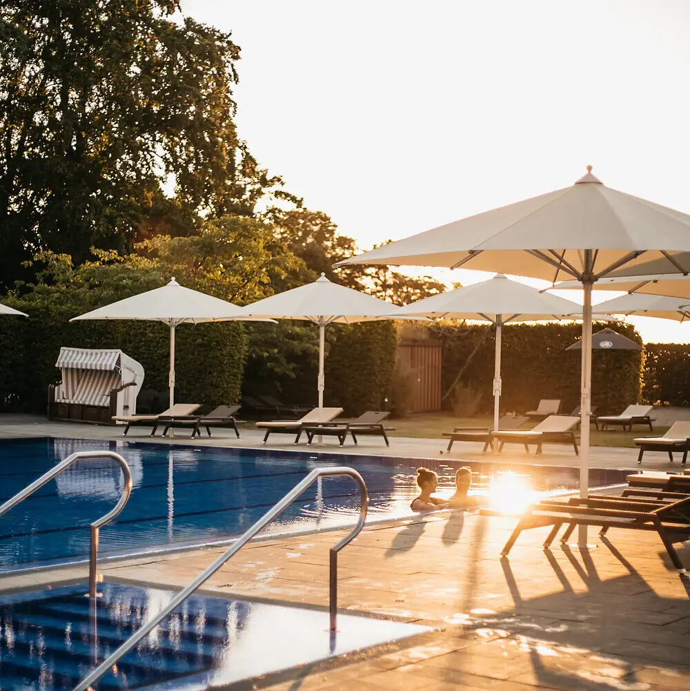 Wellness im A-ROSA Travemünde Eine Person im Pool mit Sonnenschirmen und Stühlen.