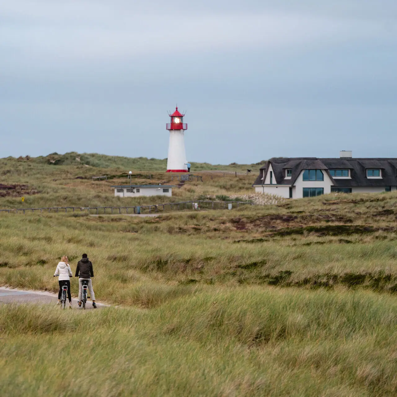 Destinationen und Orte Ein Paar fährt Fahrräder in einem grasbewachsenen Gebiet mit einem Leuchtturm im Hintergrund.
