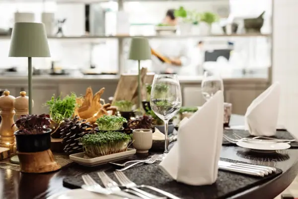 Küchentisch Der Küchentisch im A-ROSA Gothischen Haus Wernigerode mit Geschirr, einem Blumenstrauß in einer Vase und Essen.