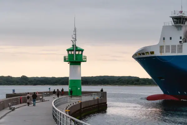 Molenfeuer in Travemünde Ein grüner und weißer Leuchtturm neben einem großen Schiff an einem Pier.