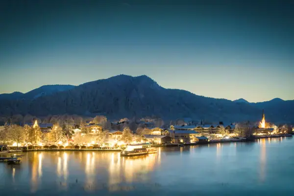 Rottacher Advent Eine Stadt am Wasser mit Bergen im Hintergrund und klarem Himmel.