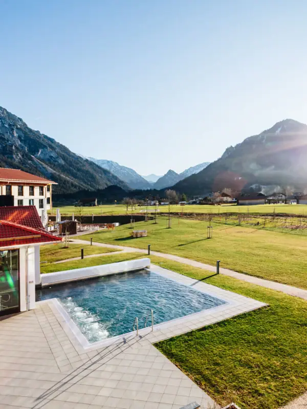 aja Ruhpolding Schwimmbecken in einer grasbewachsenen Fläche mit einem Gebäude und Bergen im Hintergrund