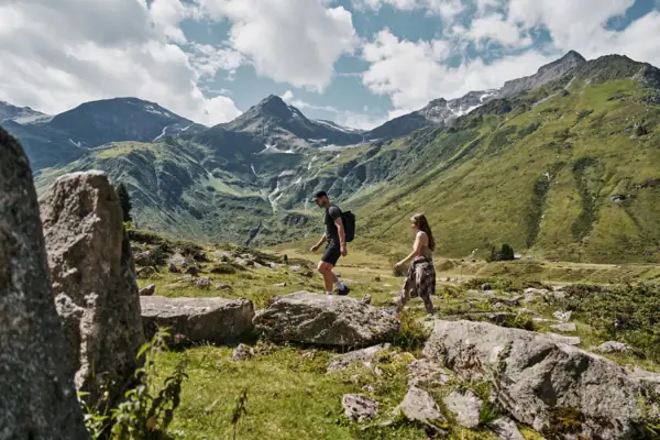 Wandern in Bad Gastein Ein Mann und eine Frau wandern auf einem felsigen Hügel mit Bergen im Hintergrund.