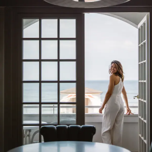 Ausblick Kurhaus Binz Eine Frau steht auf einem Balkon im A-ROSA Kurhaus Binz mit Blick auf die Ostsee und lächelt.
