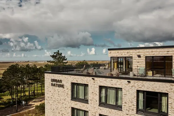 Urban Nature St. Peter-Ording Ein Gebäude mit Balkon, das auf ein Feld von Bäumen und Strand blickt.