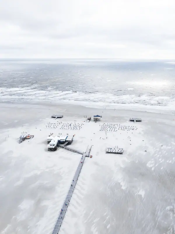St. Peter-Ording Strand von St. Peter-Ording mit einem Pier und Menschen darauf im Winter an der Nordsee.