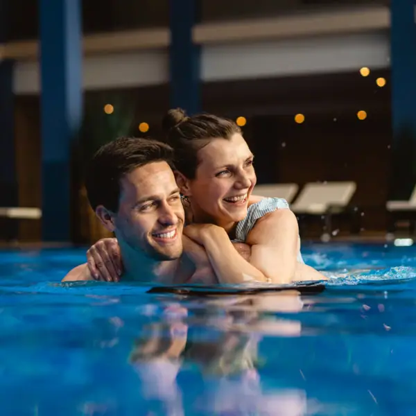 Innenpool im A-ROSA Travemünde Ein Mann und eine Frau im Pool, beide lächeln.