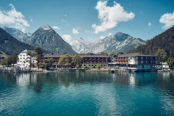 aja Fürstenhaus am Achensee Ein Gebäude neben einem Gewässer mit Bergen im Hintergrund.