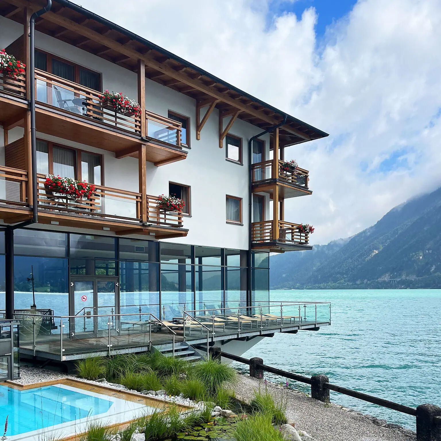 aja Hotel Achensee Ein Gebäude mit einem Pool im Vordergrund und einem Berg im Hintergrund.