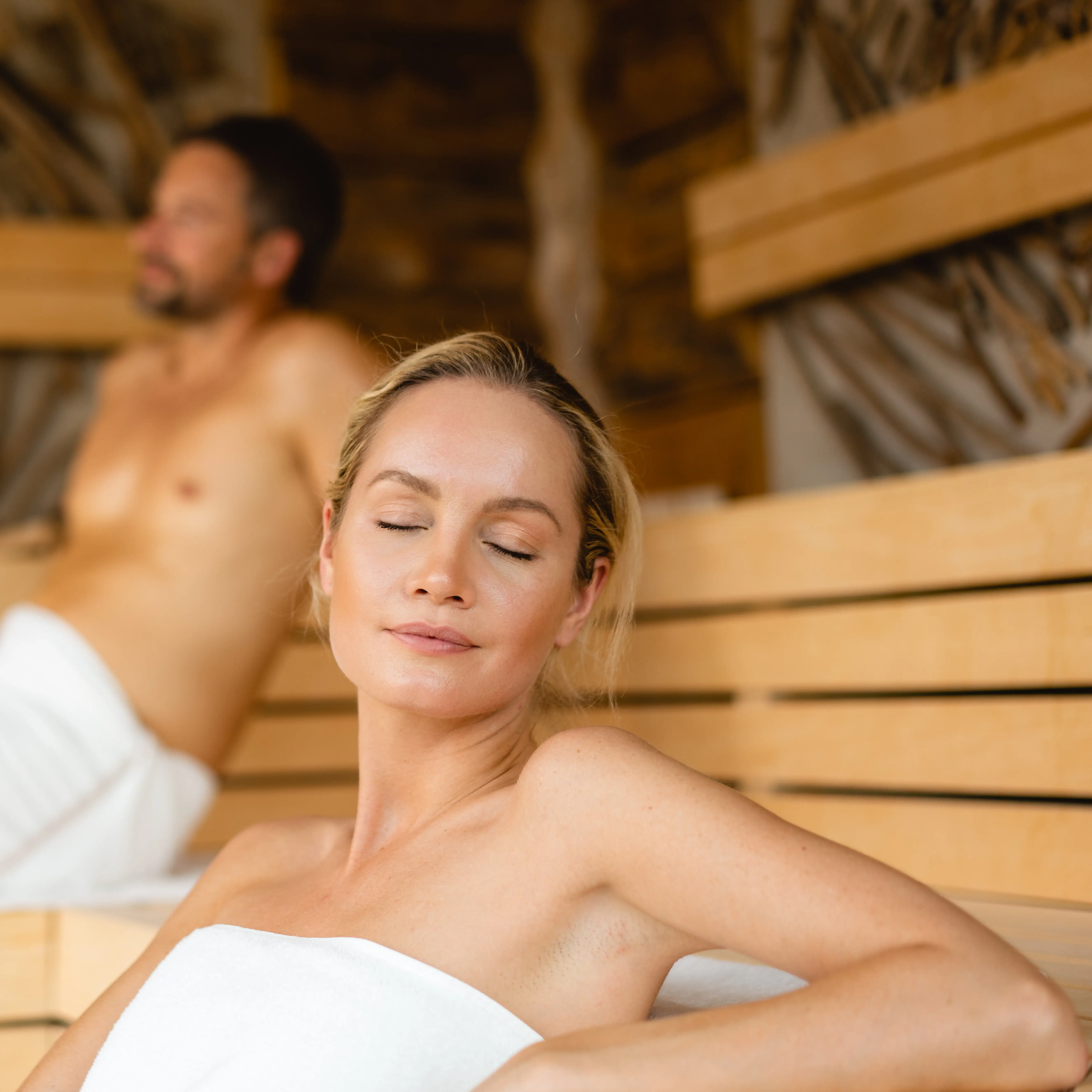 Sauna im A-ROSA Sylt Eine Frau sitzt in einer Sauna, mit einem Mann im Hintergrund.