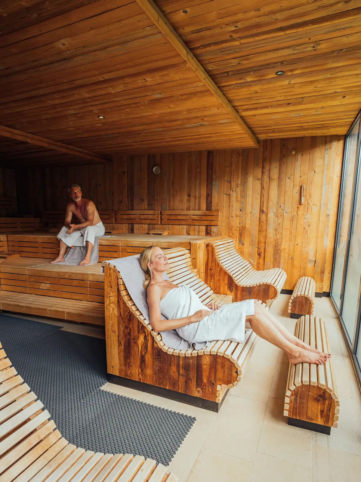 Panoramasauna A-ROSA Ifen Hotel Kleinwalsertal Eine Frau in einem Handtuch auf einer Bank in der Sauna.