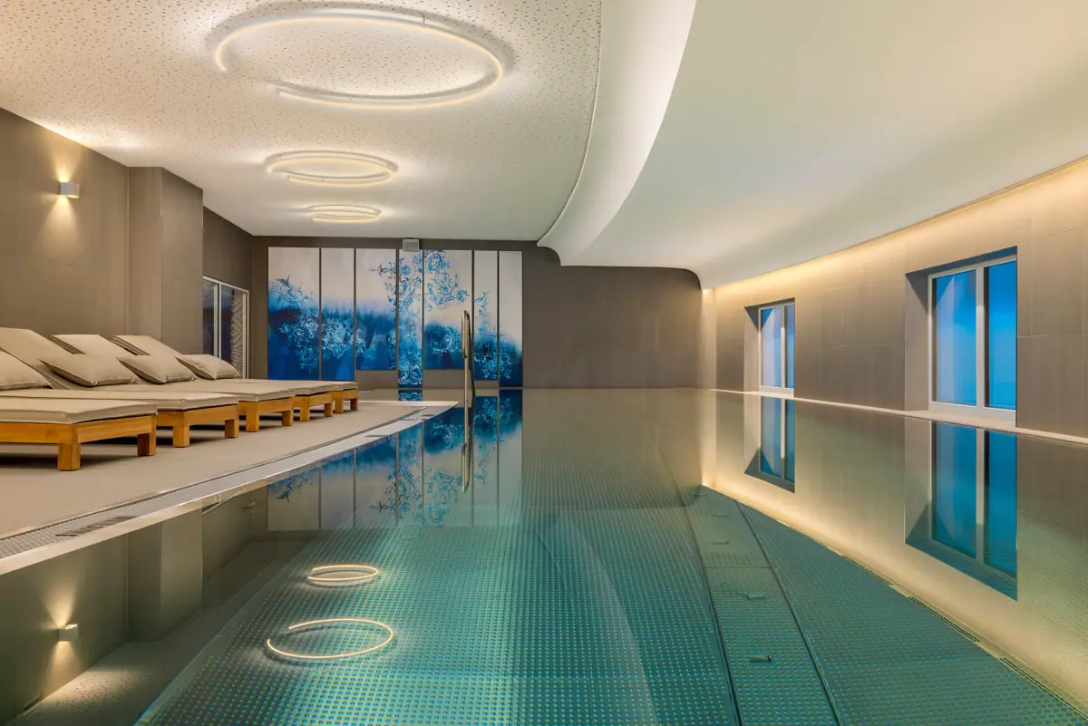 SPA-ROSA Tegernsee Ein Hallenbad mit großer Terrasse und Liegestühlen.