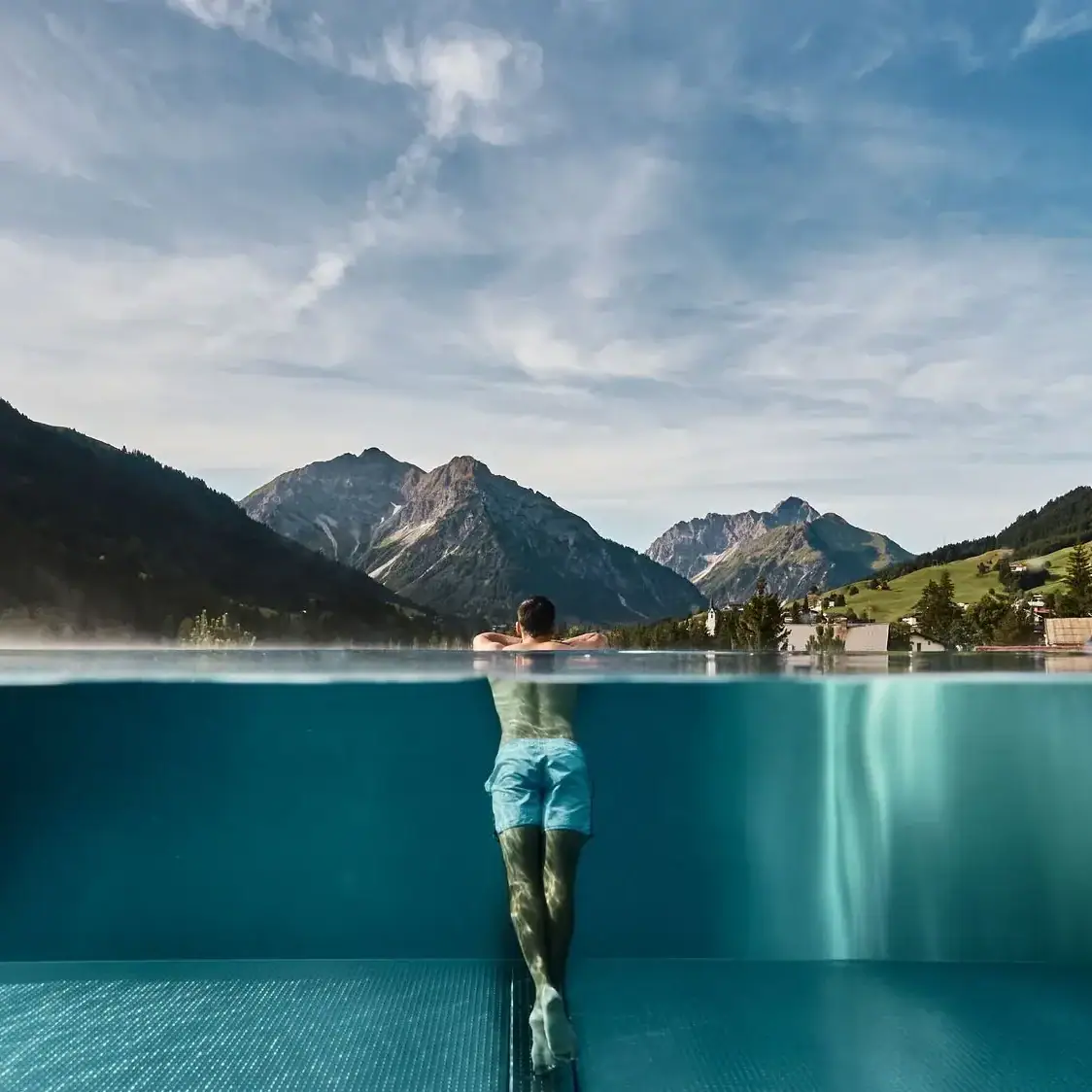 Wellness im A-ROSA Ifen Hotel Kleinwalsertal Ein Mann in einem Pool mit Bergen im Hintergrund.